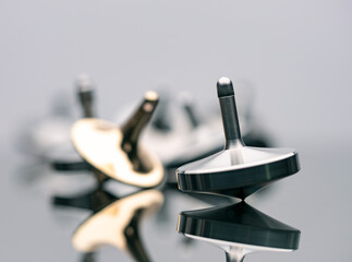 Beautiful metallic heavy spinning top spinning on mirror surface with many spinning in blur background