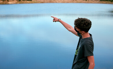 Young Caucasian man pointing in front of a blue lake