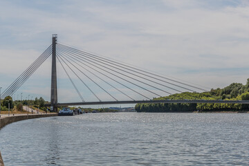 Lanaye cable-stayed bridge, which crosses the Albert Canal with boats anchored below and with green vegetation in the background, cloudy day in Belgium