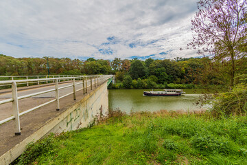 Juliana canal with its calm waters with a boat sailing towards the vehicular bridge with its white metal fence, sunny day with a blue sky with abundant white clouds in South Limburg, Netherlands