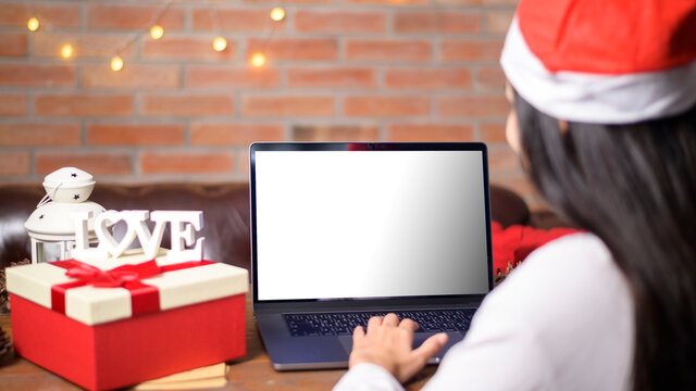 Young smiling woman wearing red Santa Claus hat making video call on social network with family and friends on Christmas day. laptop monitor screen mock up.
