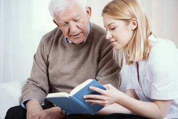 Young blonde volunteer reading book to senior man in nursing home