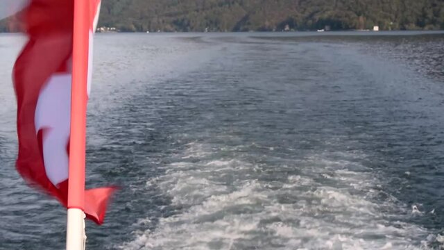 ripples left by a boat in the lake of lugano with the swiss flag waving on the side