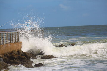 Waves crashing onto the pier with a fisherman barely visible in the wake