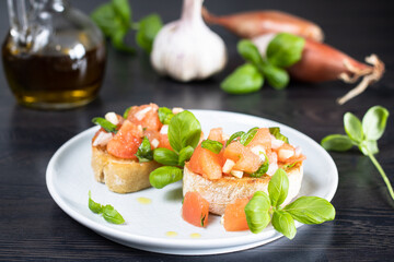 Bruschetta on a white plate with basil, onion, garlic and olive oil in the background