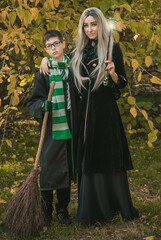 Kid and witch woman in of the magical atmosphere. Boy and mom in green robe magic in the forest. Family Halloween time