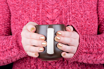 A girl in a red sweater holds a coffee cup.