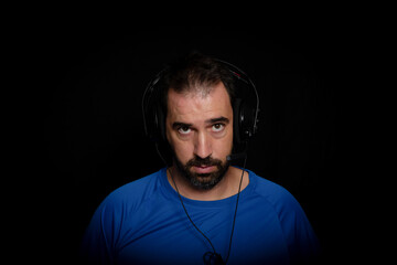 Bearded man dressed in blue t-shirt and with headphones posing on black background