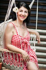 Brunette middle aged woman in red checkered dress and white flower in her hair