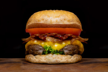 Close up fresh tasty the hamburger with cheese, tomato, beef, bacon and green salad vegetable, selective focusing technical, wooden table and darkness background.