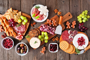Christmas theme charcuterie table scene against a dark wood background. Variety of cheese and meat appetizers. Overhead view.