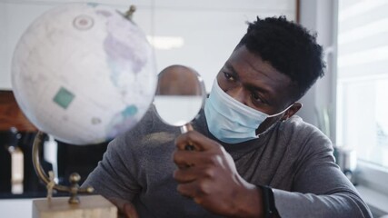 Young black man with face mask looking at the through magnifying glass. High quality 4k footage - Powered by Adobe