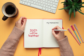 Stock photo of woman writing resolutions in a 2021 new year notebook on yellow background