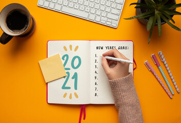 Stock photo of a young woman hand writing in a 2021 new year notebook with list of resolutions and...