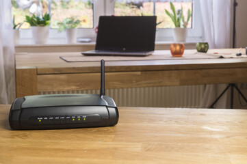 Wireless modem router network hub on a wooden table. With notebook or laptop in background.