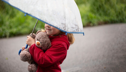 little child playing with teddy bear covered by umbrella