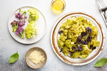 Fried green and purple cauliflower with herbs and spices on plate over gray stone background. Top view