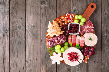 Christmas theme charcuterie board. Overhead view against a dark wood background. Mixed cheese and meat appetizers.
