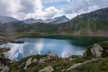 Alpine Bombasel Lake on Cermis Alps - Italy. Dolomite peaks are visible in the background and reflect in the water along with the clouds. Trentino, Italy