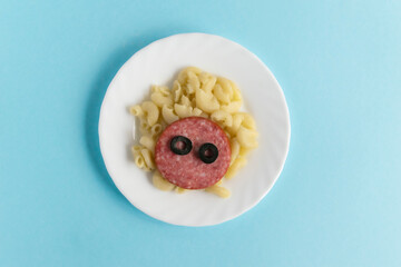 Funny Breakfast for children in the form of a bull's face made of pasta, sausage, bacon, olives and fresh tomatoes on a blue background. Instruction how to make creative food art breakfast for kids.