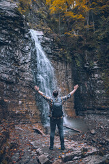 hiker man looking at autumn waterfall