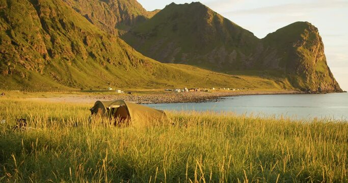Abandoned tent blowing in wind on Lofoten coast with mountains in midnight sun