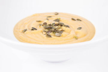 Pumpkin soup decorated with pumpkin seeds on a plate  on a white background