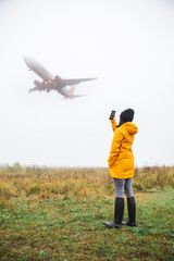 woman in yellow raincoat taking picture of the landing plane
