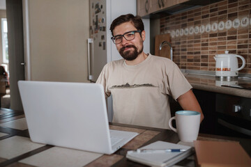 Fototapeta na wymiar Smiling hipster freelancer holding hands behind head sitting at office desk behind laptop.
