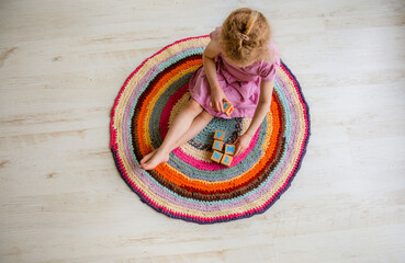 4 year old young child sit on round colorful crochet rug from repurposed T-shirts yarn on white...