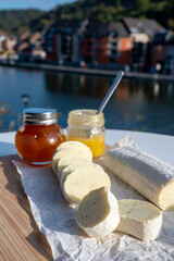 Belgian abbey cheese fagotin in pieces with jam served outdoor with view on Maas river and center of Dinant, Wallonia, Belgium