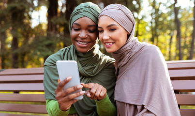Modern Muslim Woman Recommending Smartphone Mobile App To Friend Outdoor