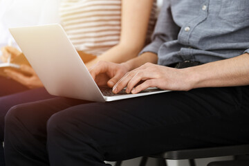 Naklejka premium Group of casual dressed business people working at meeting or conference in sunny office, close-up of hands. Businessman using laptop computer
