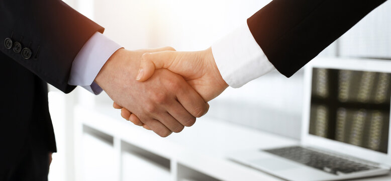 Businessman and woman shaking hands in sunny office, close-up. Concept of handshake as success symbol in business