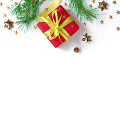 The gift wrapped in red wrapping paper is tied with a yellow ribbon with a bow. Natural pine branches, cones and gold stars are on a white background. Christmas composition. Flat lay. Copy space