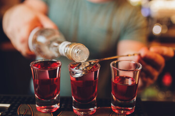 close-up of barman hand pouring alcohol into shot glasses in a nightclub or bar.