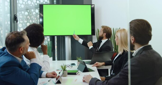 Good-looking confident purposeful multiracial colleagues holding a meeting in boardroom using digital whiteboard with chroma key green screen,close up