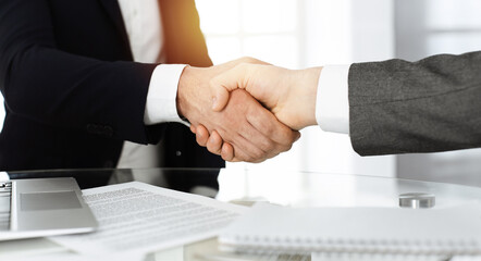 Unknown diverse business people are shaking hands finishing contract signing in sunny office, close-up. Business handshake concept