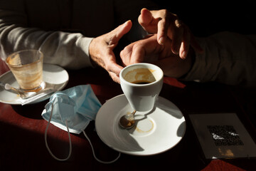 The hand of a man, that holds a cup of coffee, are lovingly picked up by his wife's, while the afternoon light enters through the bar window, Luesia, Aragón, Spain.