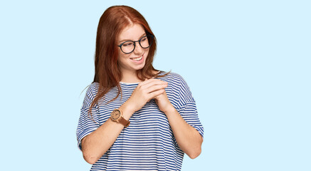 Young read head woman wearing casual clothes and glasses laughing nervous and excited with hands on...