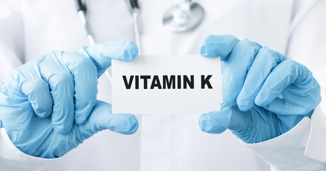 Vitamin K wrote on a card in doctor hands, close-up of gloved hands.