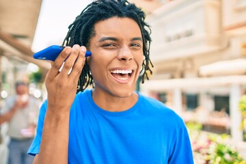 Young african american man smiling happy listening audio message using smartphone at street of city.