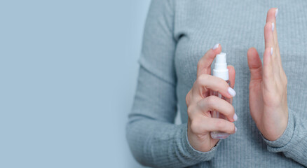 Woman holding antibacterial spray antiseptic on gray light background