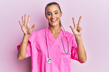 Young hispanic woman wearing doctor uniform and stethoscope showing and pointing up with fingers...