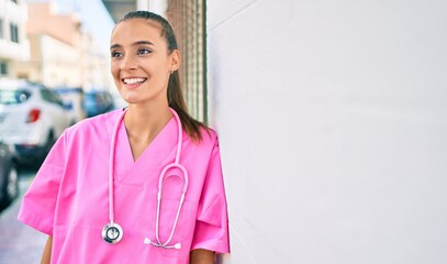 Young hispanic doctor woman smiling happy leaning on the wall at street of city.
