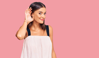 Fototapeta premium Young hispanic woman wearing casual clothes smiling with hand over ear listening an hearing to rumor or gossip. deafness concept.