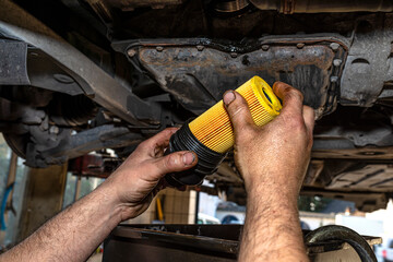 Car mechanic holding a new oil filter for a diesel engine in the background oil pan from the engine.