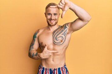 Fototapeta premium Young caucasian man wearing swimwear shirtless smiling making frame with hands and fingers with happy face. creativity and photography concept.