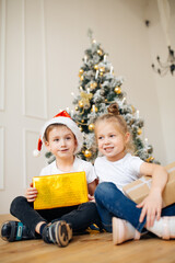 Obraz na płótnie Canvas Two happy children brother and sister in Christmas hats with gift boxes. New year tree, christmas concept
