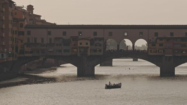 Panorama of ancient city of Florence and bridge with crowd of people. Close up of alone boat or gandola floating along river channel and under arches of bridge. Architectural art or culture concept.